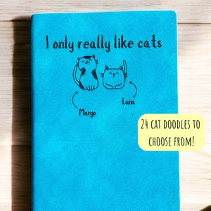 Puede incluir: Una libreta azul con el texto "I only really like cats" y dos ilustraciones de gatos con los nombres "Margo" y "Luna" escritos debajo. El texto "24 cat doodles to choose from!" está escrito en un rectángulo amarillo.