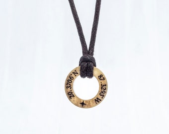 May include: A gold-colored necklace with a round pendant featuring the coordinates "20.3706° N, 87.3293° W" engraved on it. The necklace is made of a black cord.