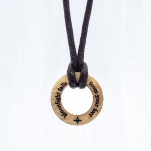 May include: A wooden ring necklace with a black cord. The ring has the words "Moonlight falls from your feet" engraved on it.