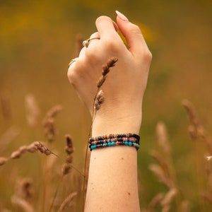 Three personalised beaded Morse code bracelets, made from black, natural and colourful beads. Pictured on ladies wrist with corn crop background.