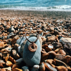 Brown waxed cotton and vegan ivory wave necklace pictured on large stone with crashing waves in the background.