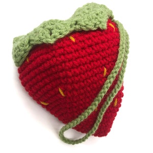 May include: A handmade crochet strawberry-shaped pouch. The pouch is primarily red with green leaves and a green drawstring. Yellow stitches are scattered across the red body. The pouch is likely used to store small items.