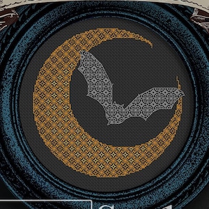 Puede incluir: Un aro de bordado negro y dorado con una luna creciente y un diseño de murciélago. El aro está enmarcado en un marco de madera azul oscuro. El texto "Harvest Moon" está escrito en una pancarta sobre el aro. El texto "Urban Stitches" está escrito debajo del aro.