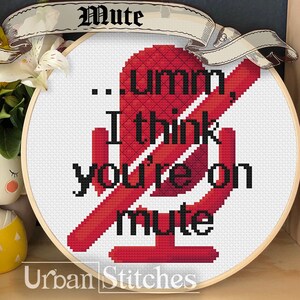 Puede incluir: Un aro de bordado de punto de cruz rojo y blanco con un icono de micrófono y el texto "...umm, I think you're on mute". El aro está sobre una superficie de madera con un girasol y una pequeña figura de muñeca.