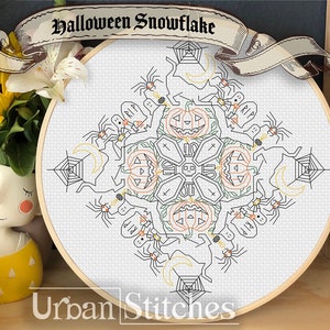 Puede incluir: Un aro de bordado blanco con un diseño de copo de nieve de Halloween en punto de cruz blanco y negro. El copo de nieve presenta calabazas, arañas y telarañas. El texto "Halloween Snowflake" está escrito en negro en una pancarta sobre el aro.