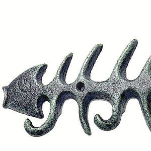 May include: A dark gray, textured cast iron wall hook shaped like a fish skeleton. The design features a horizontal spine with multiple protruding ribs that curve downward to form four distinct hooks for hanging items, with two mounting holes.