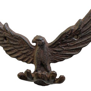 May include: A cast iron eagle wall hook with outstretched wings. The eagle is a dark brown color with detailed feathering and two holes for mounting. The hook is designed to be mounted on a wall and used for hanging items.