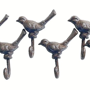 May include: Six decorative cast iron bird hooks. Each hook features a detailed bird perched above a curved hook. The hooks are finished in a rustic brown color, perfect for adding a touch of nature-inspired decor to any space.