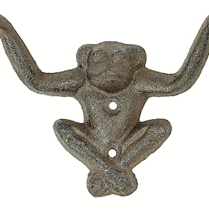 May include: A cast iron monkey hook with outstretched arms, perfect for hanging towels or coats. The hook is painted in a dark brown color and has a rustic finish.