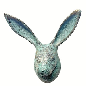 May include: A wall-mounted hare head sculpture featuring a textured, weathered finish in shades of teal, green, and bronze. The hare has long, upright ears and a detailed facial structure, presented as a decorative object with a rustic appearance.