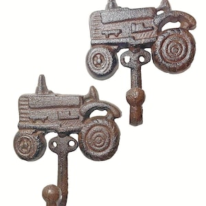 May include: Two rustic brown cast iron tractor-shaped wall hooks. Each hook features a detailed tractor design with wheels, a cab, and a hook for hanging items. Perfect for a farmhouse or country-themed decor.