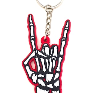 May include: A red skeleton hand keychain with a silver key ring and chain. The hand is making the rock and roll hand gesture.