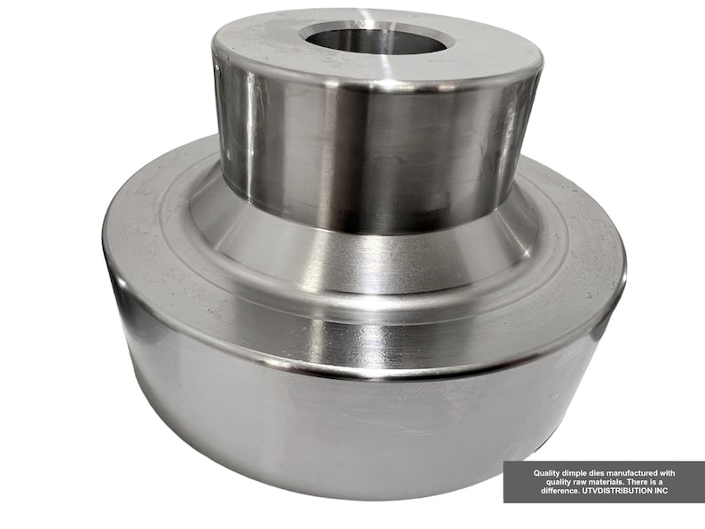 May include: A silver metal dimple die with a round top and a flat bottom. The die has a smooth, polished surface.