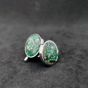 May include: A pair of silver cufflinks with a green circuit board design. The cufflinks are round and have a shiny finish.