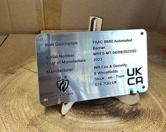 Può includere: Una targhetta identificativa rettangolare in metallo color argento con angoli arrotondati e quattro fori di montaggio. La targhetta presenta testo stampato in nero, tra cui Item Description FAAC B680 Automated Barrier, Serial Number WRFS-MT-04/09/2023/02, Year of Manufacture 2023 e i dettagli del produttore WR Fire & Security.