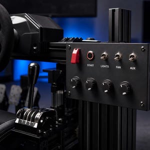 May include: A black racing simulator control panel featuring a red safety toggle switch, a start button, and three metal toggle switches labeled START, LIGHTS, FAN, and AUX. Below are four black rotary knobs mounted on a vertical aluminum frame.