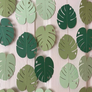 K&ouml;nnte beinhalten: Girlanden aus gr&uuml;nen Papierbl&auml;ttern in verschiedenen Schattierungen, von hell bis dunkel. Die Bl&auml;tter in Monstera-Form sind aufgereiht und bilden ein tropisches Thema. Jedes Blatt hat ein gen&auml;htes Aussehen.