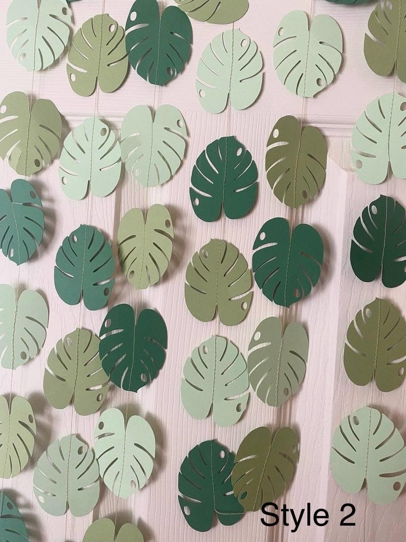 Puede incluir: Una guirnalda de hojas de Monstera de papel en varios tonos de verde. Las hojas est&aacute;n cortadas con patrones de venas detallados y ensartadas. El texto "Style 2" es visible en la parte inferior.