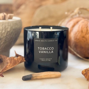 Puede incluir: Un tarro de vela de vidrio negro con una etiqueta blanca que dice "Urban Melts Candle Co. Tobacco Vanilla Candle Bougie 18oz | 510g".