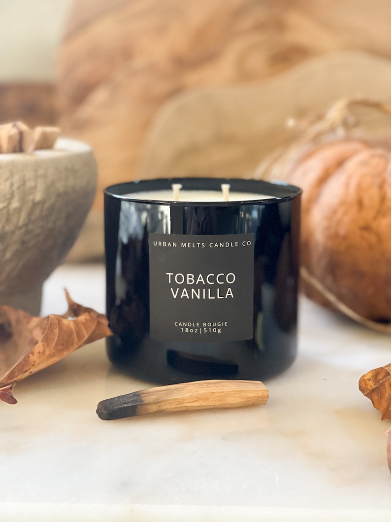 Puede incluir: Un tarro de vela de vidrio negro con una etiqueta blanca que dice "Urban Melts Candle Co. Tobacco Vanilla Candle Bougie 18oz | 510g".