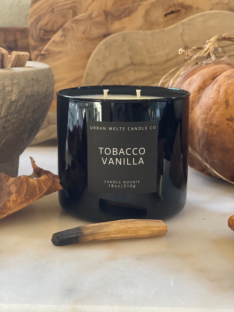 Puede incluir: Vela negra de vidrio con una etiqueta blanca que dice "Urban Melts Candle Co. Tobacco Vanilla Candle Bougie 18oz | 510g"