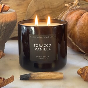Puede incluir: Un tarro de vela de vidrio marr&oacute;n oscuro con dos mechas y una etiqueta que dice "Urban Melts Candle Co. Tobacco Vanilla Candle Bougie 18oz | 510g".