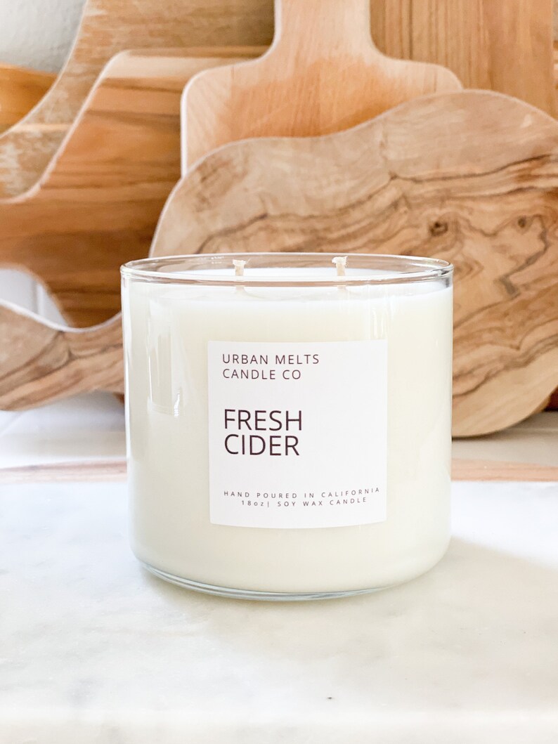 May include: A clear glass candle jar with a white label that reads "URBAN MELTS CANDLE CO" and "FRESH CIDER". The label also states "HAND POURED IN CALIFORNIA 18oz SOY WAX CANDLE".