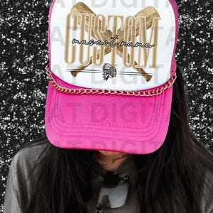 Puede incluir: Gorra de camionero rosa con malla blanca en la parte posterior. La parte delantera de la gorra presenta un diseño personalizado con dos bates de béisbol cruzados y el texto "CUSTOM mascot name".