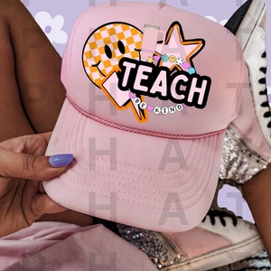 Op de afbeelding: Roze trucker cap met een gele smiley, een ster en het woord "TEACH" in roze letters. De pet heeft ook de woorden "BE KIND" in kleinere letters.