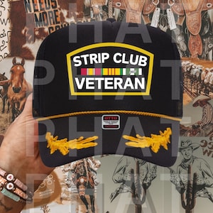 Peut inclure: Un chapeau de camionneur noir avec un patch jaune qui dit "Strip Club Veteran". Le patch a une rangée de rubans colorés dessus. Le chapeau a une visière jaune et un motif brodé jaune au dos.