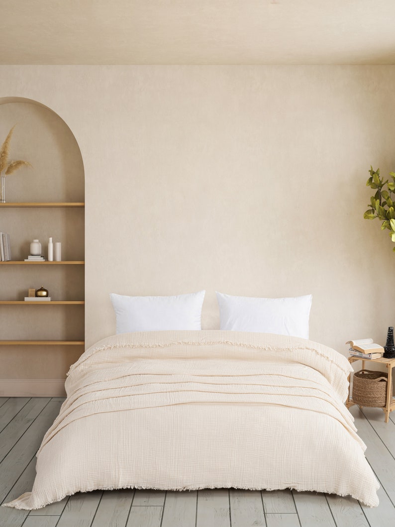 May include: A cream-coloured textured duvet cover with frayed edges draped over a bed. Two plain white rectangular pillows are positioned at the head of the bed. The fabric features a visible grid-like weave pattern throughout the entire surface.