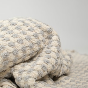 May include: A folded terry cloth towel featuring a textured, repeating pattern of small, raised grey dots against an off-white background. The fabric has a soft, looped pile construction, creating a tactile surface with a consistent color scheme.