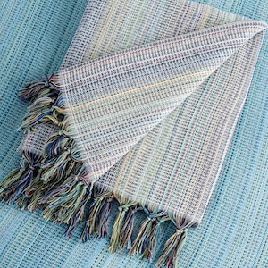 May include: A folded blue and white striped throw blanket with fringe tassels. The blanket is made of a soft, woven fabric.
