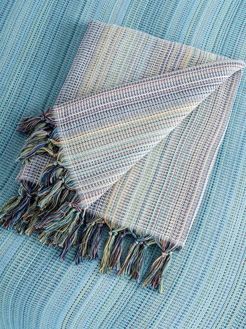 May include: A folded blue and white striped throw blanket with fringe tassels. The blanket is made of a soft, woven fabric.