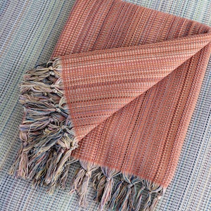May include: A folded orange and brown striped throw blanket with multicolored fringe tassels.
