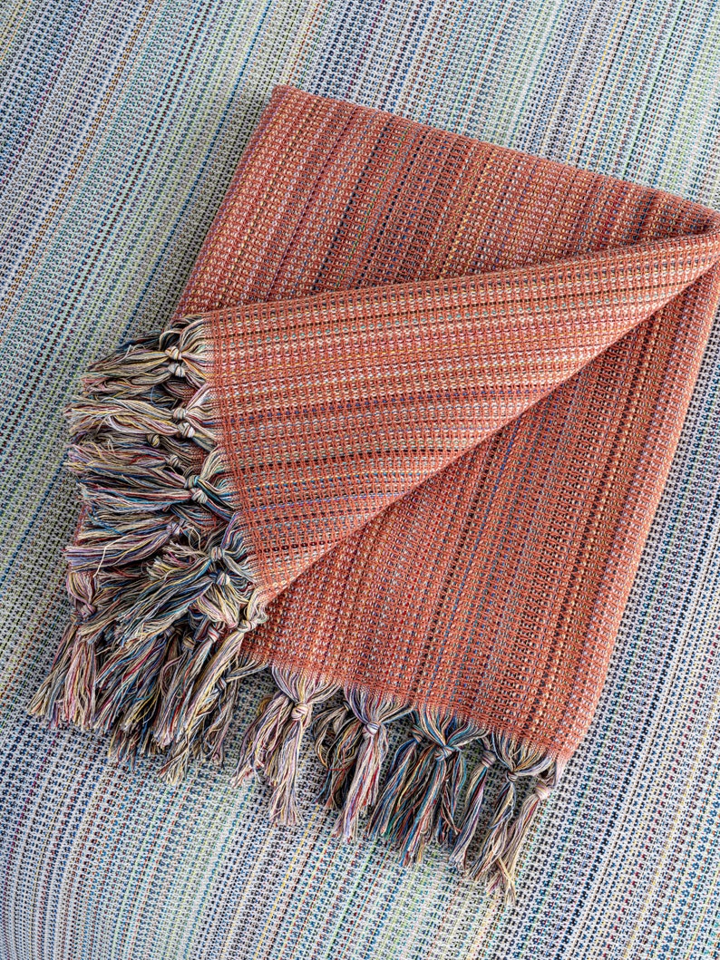 May include: A folded orange and brown striped throw blanket with multicolored fringe tassels.