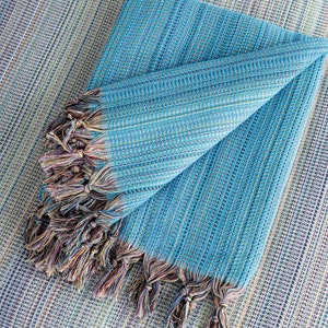 May include: A folded blue and white striped throw blanket with fringe tassels. The blanket is made of a soft, woven fabric.