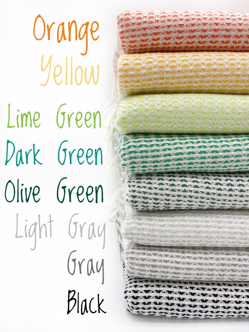 May include: A stack of eight folded woven textiles with fringe, featuring a repeating geometric pattern. The colors from top to bottom are orange, yellow, lime green, dark green, olive green, light gray, gray, and black, with corresponding text labels.