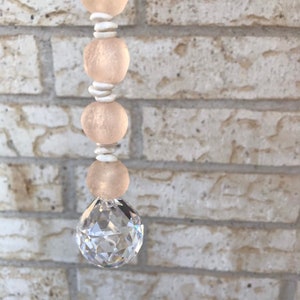 May include: A crystal suncatcher with a pink and white beaded chain. The beads are made of glass and have a frosted finish.
