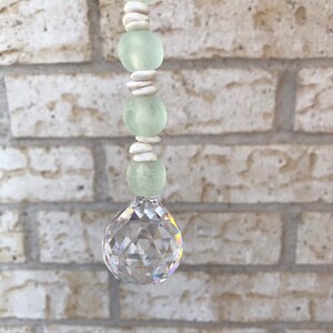 May include: A crystal suncatcher with a clear crystal ball and a beaded string of white and light green beads.