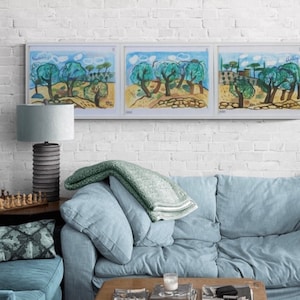 May include: Three framed landscape paintings with olive trees and the word "Italy" in the top right corner. A blue sofa with pillows and a green blanket is below the paintings. A gray lamp and a chess set are on the left.