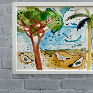 May include: A framed watercolor painting of a beach scene with two palm trees, blue water, and white birds. The painting is in a white frame and is hanging on a white brick wall.