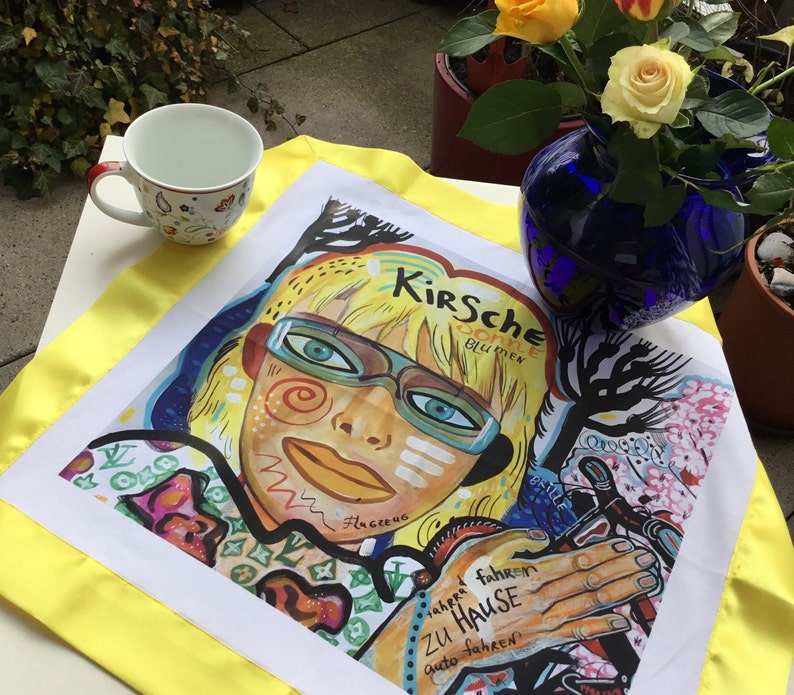 Pode incluir: Uma toalha de cozinha branca com uma borda amarela apresenta uma ilustra&ccedil;&atilde;o colorida de uma pessoa com um rosto amarelo e vermelho brilhante, usando &oacute;culos e uma camisa vermelha e verde. O texto "Kirsche Blume" &eacute; vis&iacute;vel no canto superior direito da imagem. A toalha de cozinha &eacute; uma &oacute;tima adi&ccedil;&atilde;o a qualquer cozinha.
