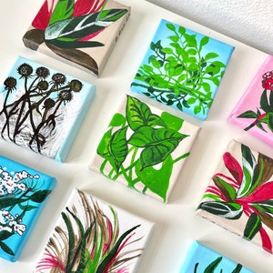 May include: A collection of eight small, square canvases with painted floral and plant designs. The canvases are painted in various shades of green, blue, red, and white. The designs include a variety of flowers, leaves, and branches.