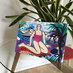 Puede incluir: Una pintura colorida de una mujer en un traje de ba&ntilde;o rosa sentada en una playa con un yate en el fondo. La pintura est&aacute; hecha en un estilo gr&aacute;fico audaz con colores brillantes y formas simples.