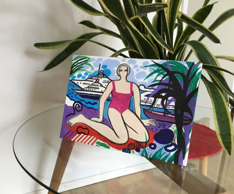 Puede incluir: Una pintura colorida de una mujer en un traje de ba&ntilde;o rosa sentada en una playa con un yate en el fondo. La pintura est&aacute; hecha en un estilo gr&aacute;fico audaz con colores brillantes y formas simples.