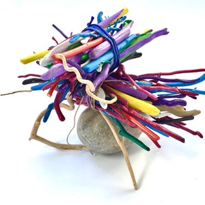 May include: A colorful sculpture made of painted sticks and a gray stone. The sticks are arranged in a radial pattern around the stone, creating a whimsical and abstract design.
