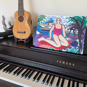 Puede incluir: Una pintura colorida de una mujer en un traje de ba&ntilde;o rosa sentada en una playa con un yate en el fondo. La pintura est&aacute; hecha en un estilo gr&aacute;fico audaz con colores brillantes y l&iacute;neas gruesas.