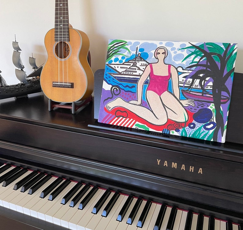Puede incluir: Una pintura colorida de una mujer en un traje de ba&ntilde;o rosa sentada en una playa con un yate en el fondo. La pintura est&aacute; hecha en un estilo gr&aacute;fico audaz con colores brillantes y l&iacute;neas gruesas.