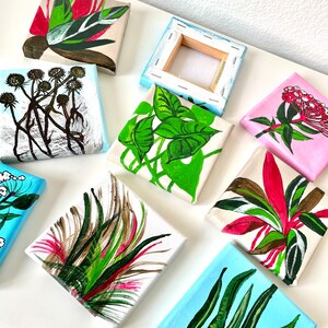 May include: Nine small canvas paintings with various botanical illustrations. The paintings feature different plants and flowers in shades of green, pink, red, and brown. The paintings are all on white canvases with a wooden frame.